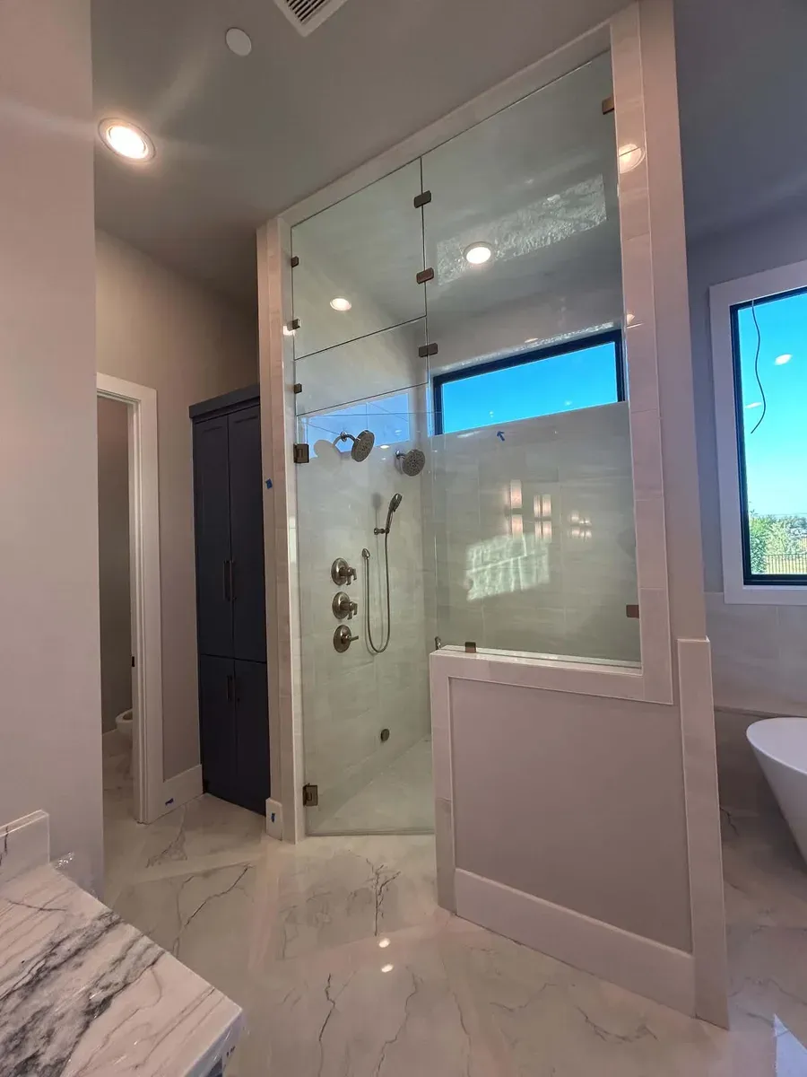 Large frameless glass walk in shower with a transom window, tiled walls and a half wall