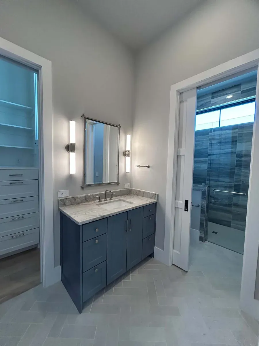 Navy blue vanity with a stone top, framed mirror and wall sconces next to a walk in closet