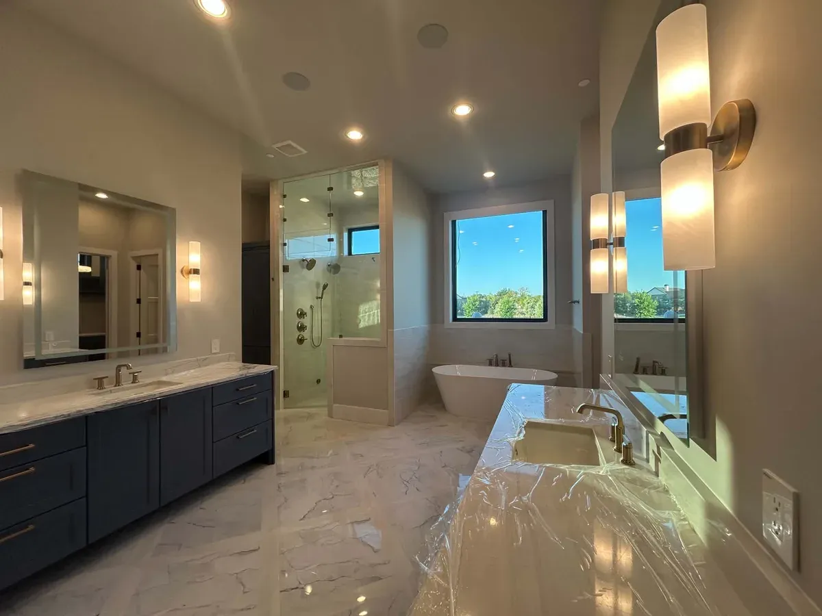 Remodeled primary bathroom with a navy double vanity, a glass walk in shower and a freestanding soaking tub