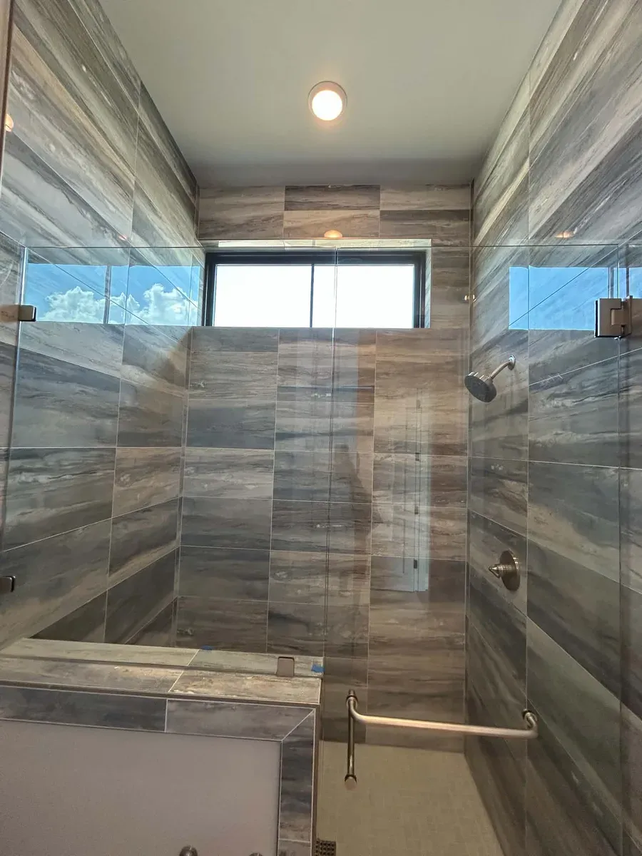 Tiled walk in shower with a built in bench, glass panel and a high window