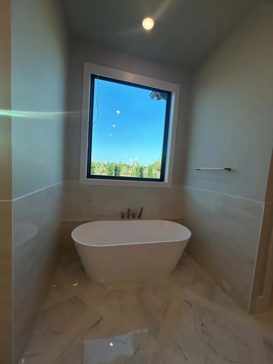 Freestanding white soaking tub under a large picture window with marble look floor tile