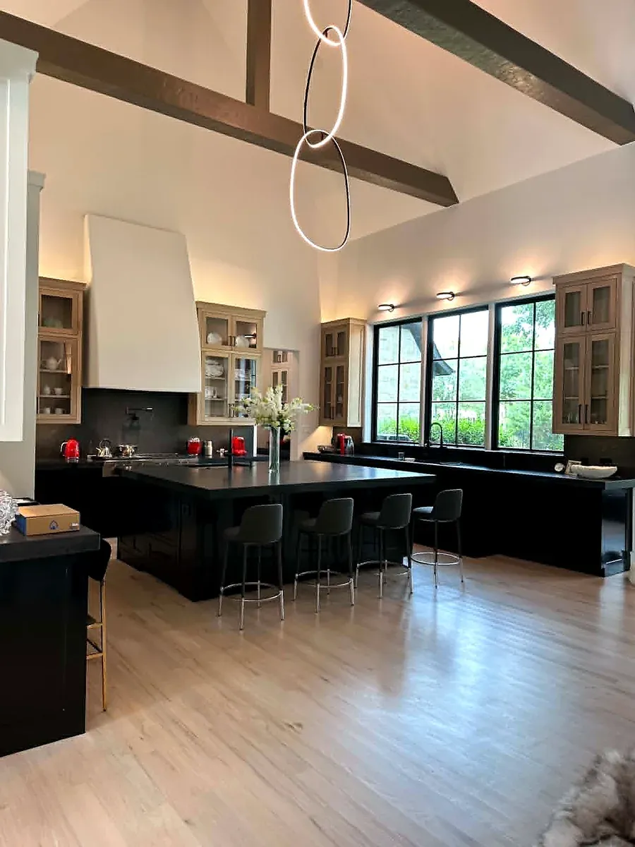 Kitchen with a vaulted beamed ceiling, a black island, glass front cabinets and a ring pendant light