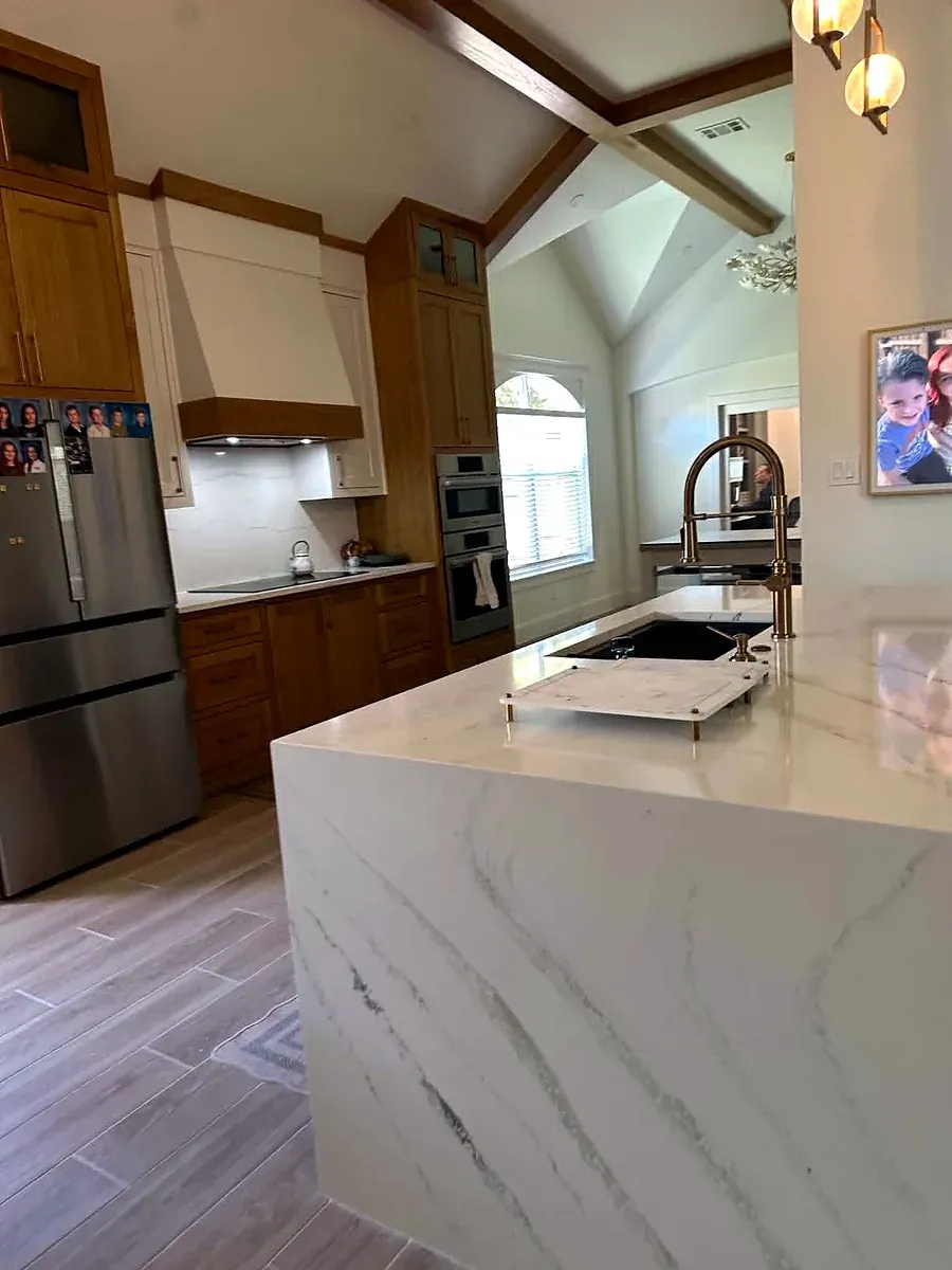 Kitchen with a white marble look waterfall island, wood cabinets and a vaulted beamed ceiling