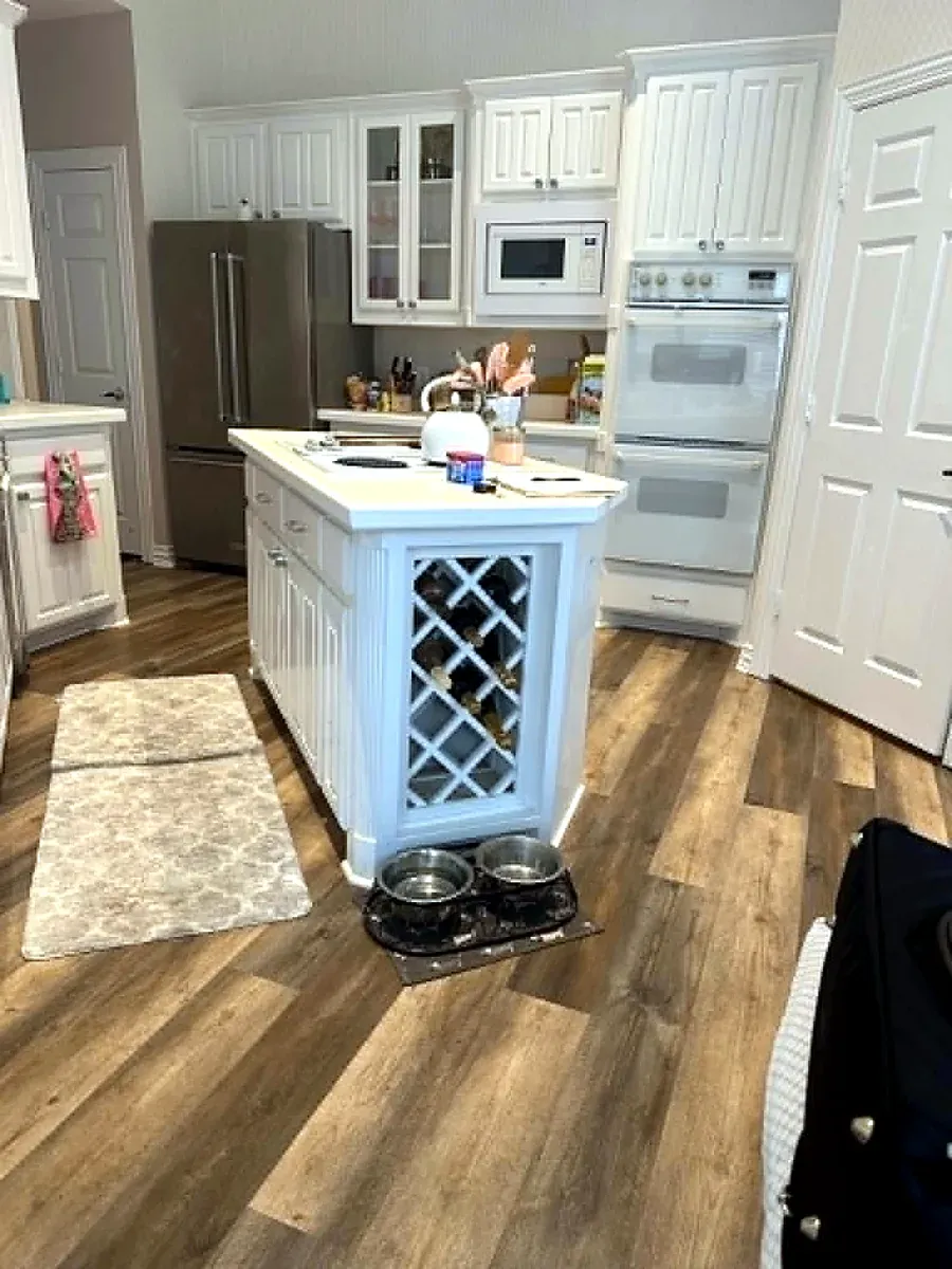 White kitchen island with a built in wine rack, white cabinets and double wall ovens