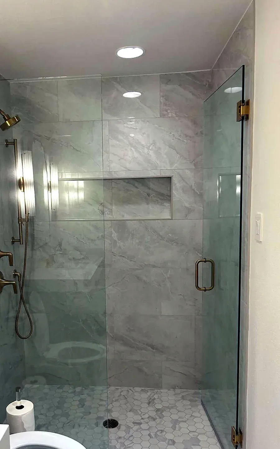 Walk in shower with marble tile walls, a recessed niche and brass fixtures